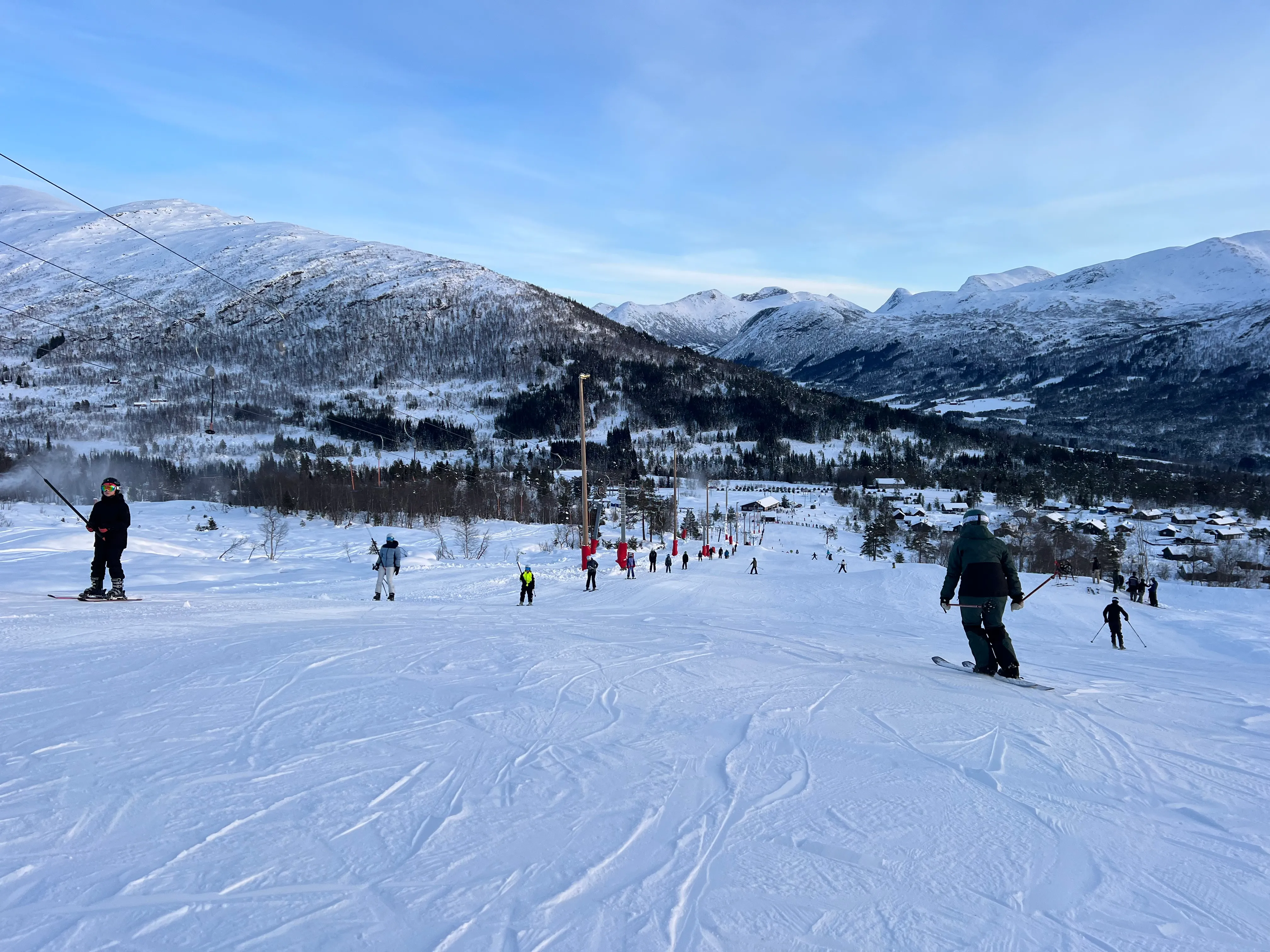 Skifolk i nedfarten med utsikt over fjell og bygd — alpint ved Hornindal Skisenter, Nordfjord og Sunnmøre